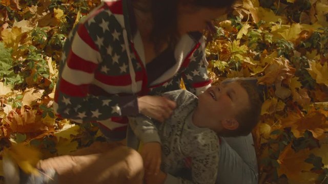 A young Caucasian woman tickles her son in autumn leaves. Recorded in Raw on Blackmagic camera.