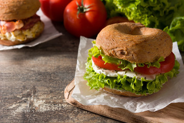 Vegetable bagel sandwich with tomato, lettuce, and mozzarella cheese on wooden table. Copy space	