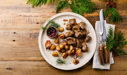 Stewed wild Venison in sauce with roast potatoes and berry sauce on wooden table copy space