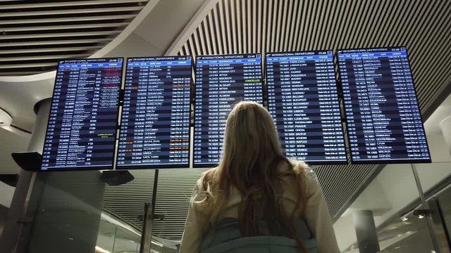 Woman in international airport near flight information board. Girl looks at the information board at the airport.