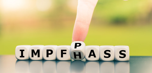 Hand dreht einen Würfel und ändert das Wort Impfhass in Impfpass.