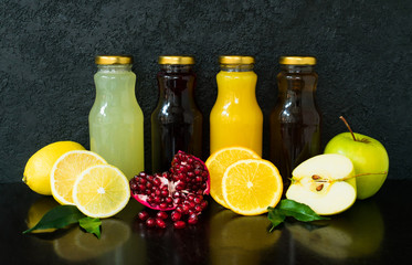 Four types of juice  in glass bottles on a black wooden background.	