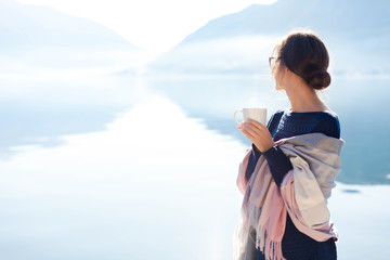 Woman drinks morning coffee at sea beach. Cozy winter picnic. Girl enjoying calm nature, travel,...