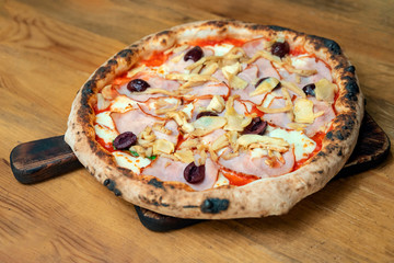 Freshly baked pizza with cheese, sauce, vegetables and meat on a wooden table