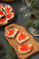 Sandwiches with red caviar are located on a wooden board against a dark background. Festive snack
