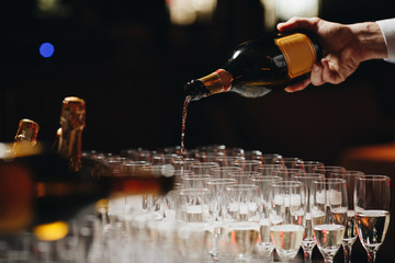 Bartender pouring champagne or wine into wine glasses on the table at the outdoors solemn wedding ceremony