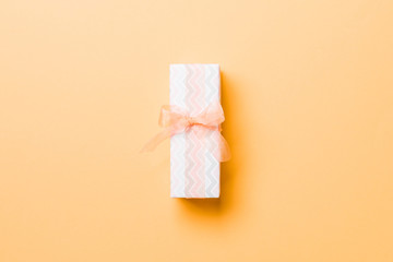 wrapped Christmas or other holiday handmade present in paper with orange ribbon on orange background. Present box, decoration of gift on colored table, top view with copy space