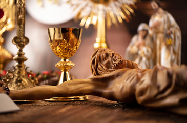 Catholic concept background.  The Cross, monstrance, Jesus figure, Holy Bible and golden chalice on the rustic wooden table.