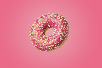 Donut with icing and sugar sprinkles on a pink background.