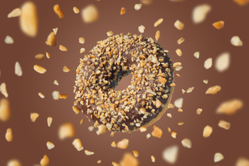 Delicious chocolate donut on a brown background with the effect of falling crushed nuts.