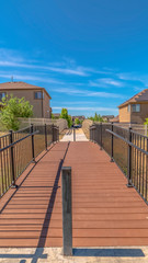 Vertical Sunny day view of bridge with brown deck and metal handrails over grassy terrain