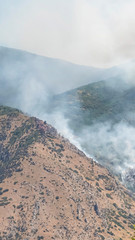 Vertical Nature landscape with puffs of white smoke rising from mountain forest fire