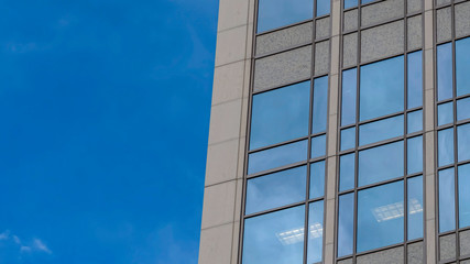 Fototapeta na wymiar Pano frame Focus on a modern building exterior with glass windows reflecting the blue sky