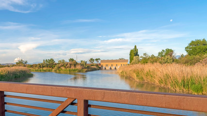Pano frame Lake with grassy shore against buildings mountain and sky viewed from a bridge