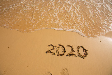 Summer beach holiday 2020 season golden sand - year - decade - new season lettering on the beach with wave and clear blue sea. Numbers 2020 year on the sea shore, message handwritten New Years concept