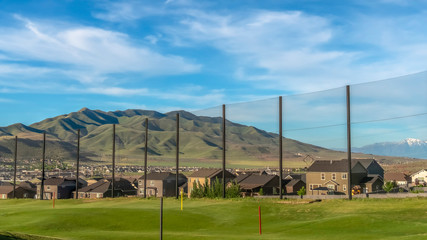 Fototapeta na wymiar Pano Gold course views with colorful flagsticks against a fence under blue sky