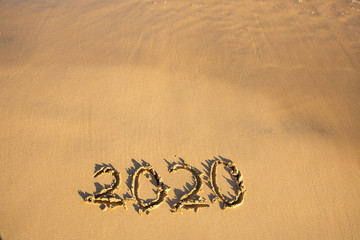 2020 summer beach holiday season written on golden sand - new season lettering on sand - numbers 2020 year  travel vacation - washed away