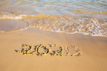 2020 summer beach holiday season written on golden sand - new season lettering on sand - numbers 2020 year  travel vacation - washed away