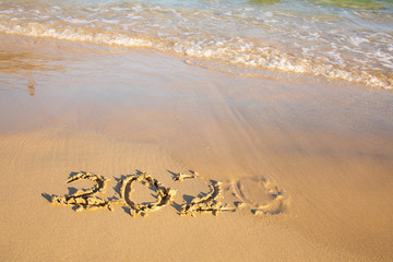 2020 summer beach holiday season written on golden sand - new season lettering on sand - numbers 2020 year  travel vacation - washed away