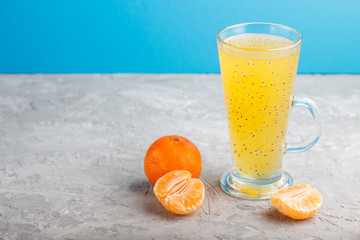 Glass of tangerine orange colored drink with basil seeds on a gray and blue background. Side view