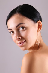 Portrait of young beautiful woman with perfectly clean face skin. Female with long black hair tied in ponytail smiling showing skincare results. Close up, copy space background.