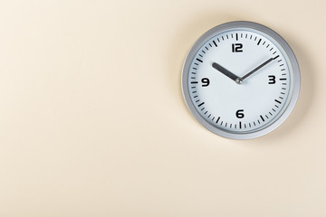 White wall clock with a yellow used hanging on the wall. Minimalist image of a wall clock on a beige background with copy space