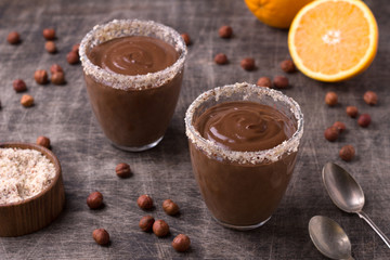 Chocolate mousse with cream, hazelnuts and orange in glasses on old dark wooden table.
