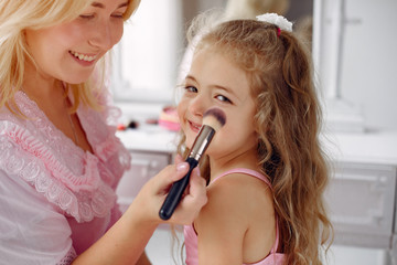 Family sitting infront a mirror. Mother in a pink pajamas. Little girl with cosmetics.