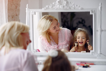 Obraz na płótnie Canvas Family sitting infront a mirror. Mother in a pink pajamas. Little girl with cosmetics.