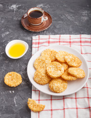 Traditional japanese rice chips cookies with honey and soy sauce on a white ceramic plate and a cup of coffee on a black concrete background. side view