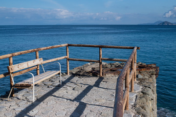 Obraz premium Empty wooden bench and fence facing the Mediterranean sea at Sant'Andrea, Elba island, Tuscan archipelago, Italy