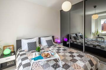 Modern interior of bedroom. Tray with food on the bed. Bedsides with round lamps.