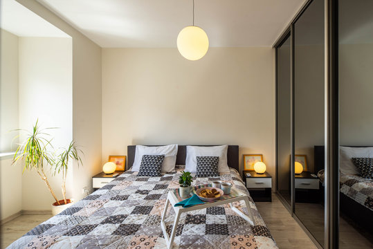 Modern interior of bedroom. Tray with food on the bed. Bedsides with round lamps.