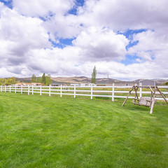 Square Spacious yard of a home with garden swing lush green grasses and white fence