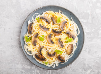 Rice noodles with champignons mushrooms, egg sauce and oregano on a gray concrete background. Top view.