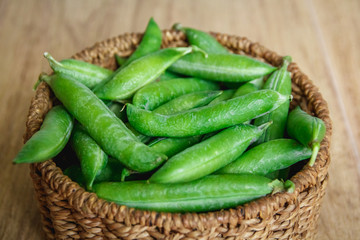 The crop of peas lies in a round wicker basket on a wooden background. Top view. Copy, empty space for text