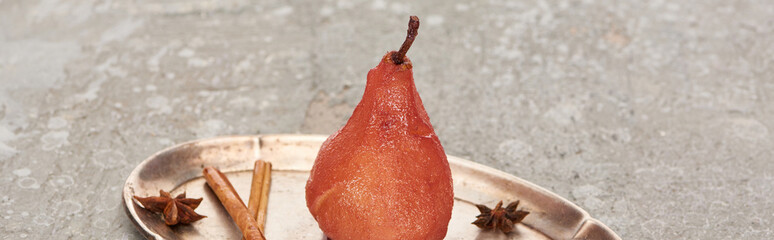 delicious pear in wine with cinnamon and anise on silver plate on grey concrete surface, panoramic...