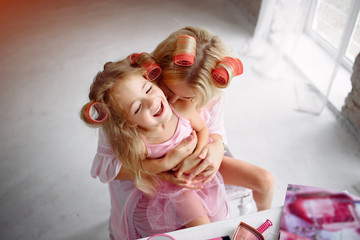 Family sitting in a room. Mother in a pink pajamas. Mom and daughter with curlers on their heads