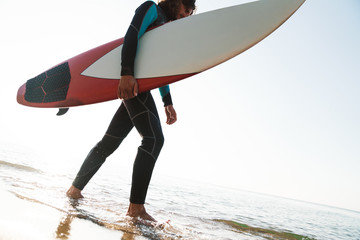 Photo of caucasian young man holding surfboard while walking