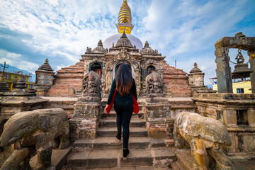 Young girl walks towards a Sacred Buddhist Monastery. Sculptures of Gods and Goddesses carved on...