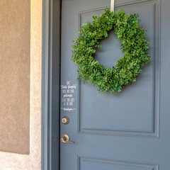 Square frame Home exetrior with close up on blue gray front door decorated with green wreath