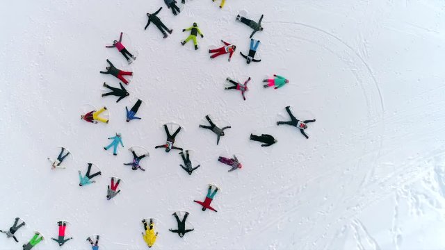Aerial: a large group of snow angels. top view on skiers making angels in the snow and lazing in the shape of a random circle. young people in bright sports clothes represent snowangel