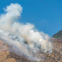 Square frame Thick puffs of smoke from fire in the mountain against clear blue sky background