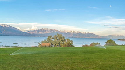 Pano Sprinklers on vast grassy terrain with blue lake snowy mountain and sky view