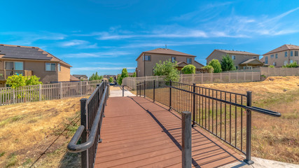 Pano frame Bridge over grassy terrain leading to houses with sunny blue sky background