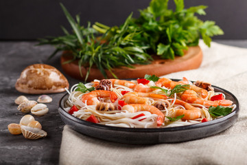 Rice noodles with shrimps or prawns and small octopuses on gray ceramic plate on a black concrete background. side view, close up.