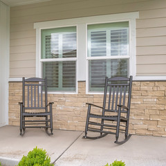 Square frame Rocking chairs against window at the porch of a home with wood and brick wall