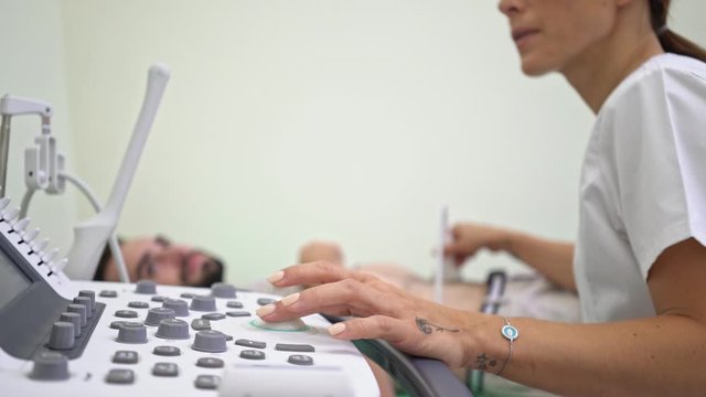 A close-up view of female doctor in medical uniform is doing abdominal ultrasound scan for young lying man at hospital