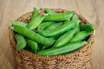 The crop of peas lies in a round wicker basket on a wooden background. Top view. Copy, empty space for text