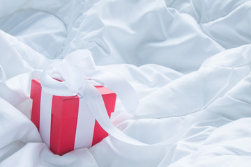 Red gift box with a white satin bow on the blanket with pleats